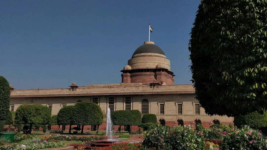 Rashtrapati Bhavan in New Delhi behind trees and a garden fountain
