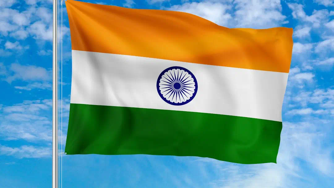 The national flag of India waving on a metal pole against a blue sky
