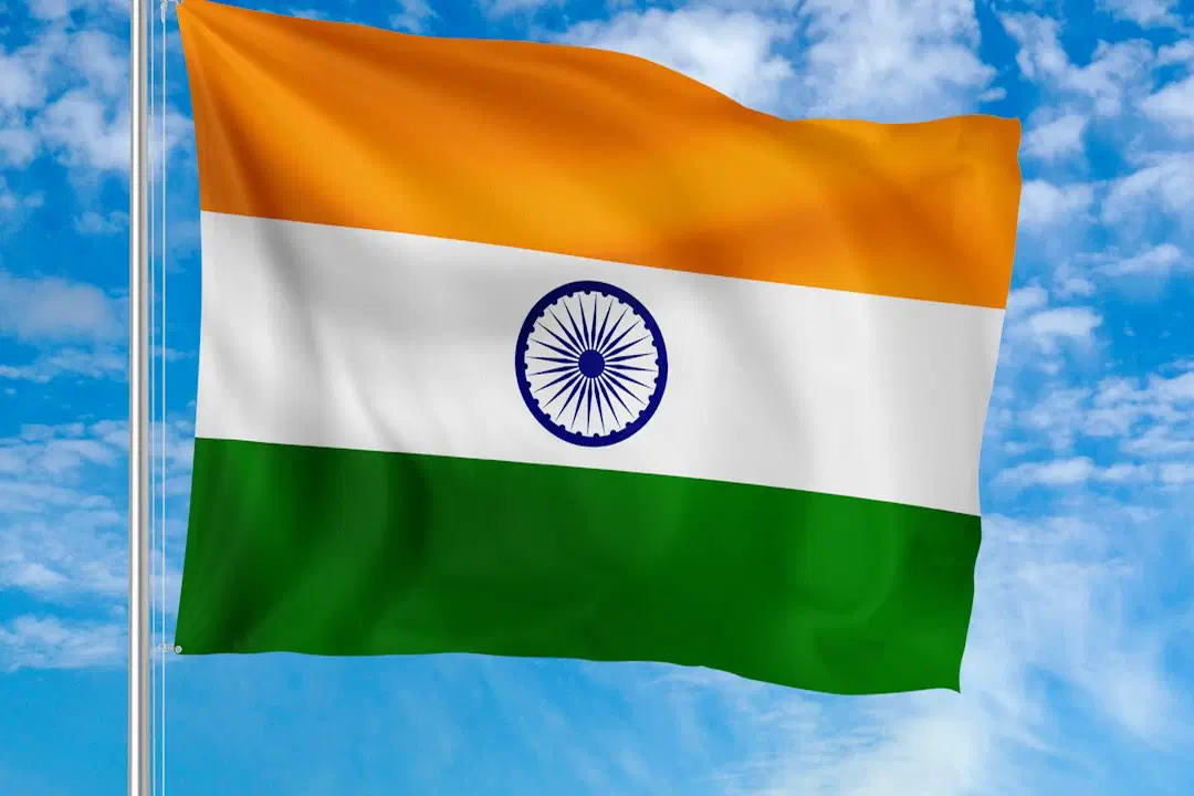 The national flag of India waving on a metal pole against a blue sky