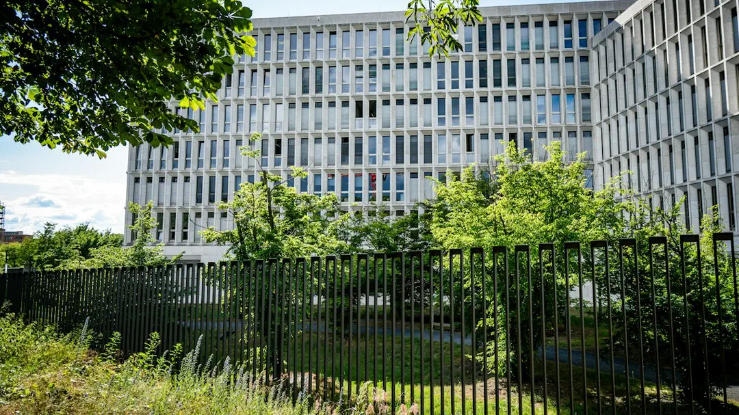 A large modern building with many windows behind a dark fence