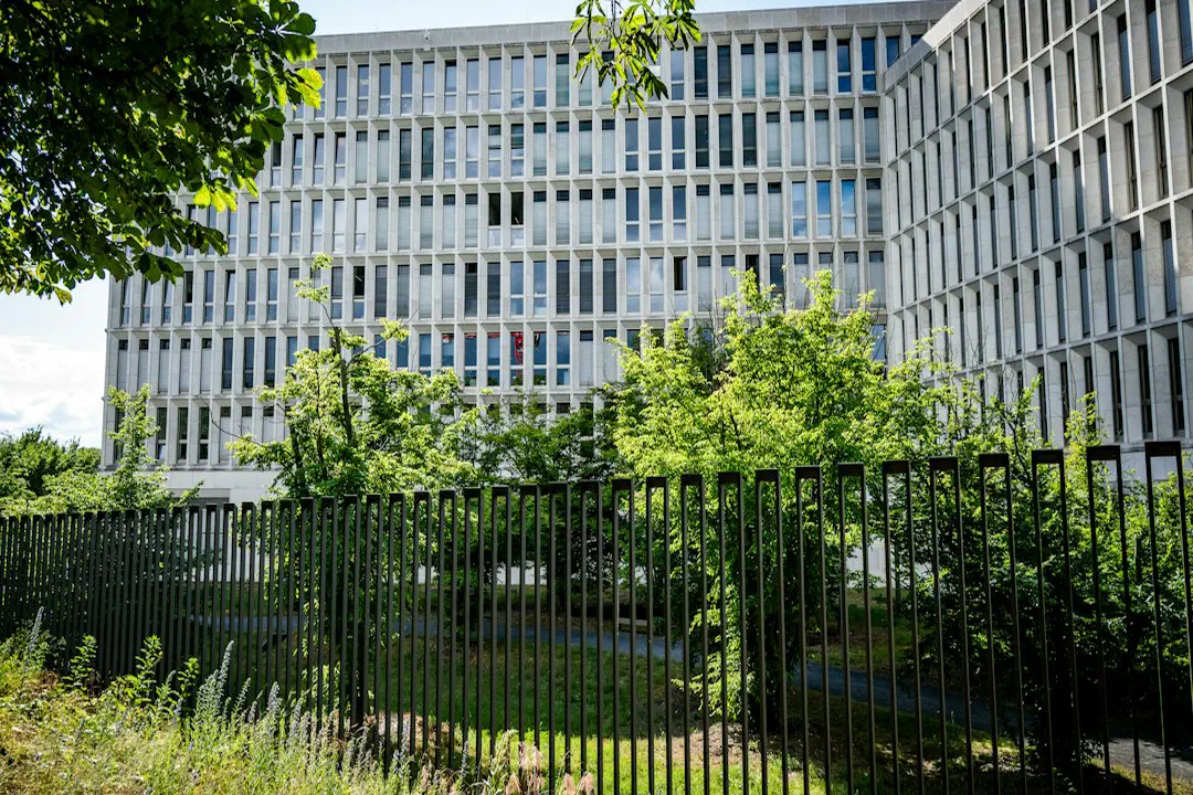 A large modern building with many windows behind a dark fence