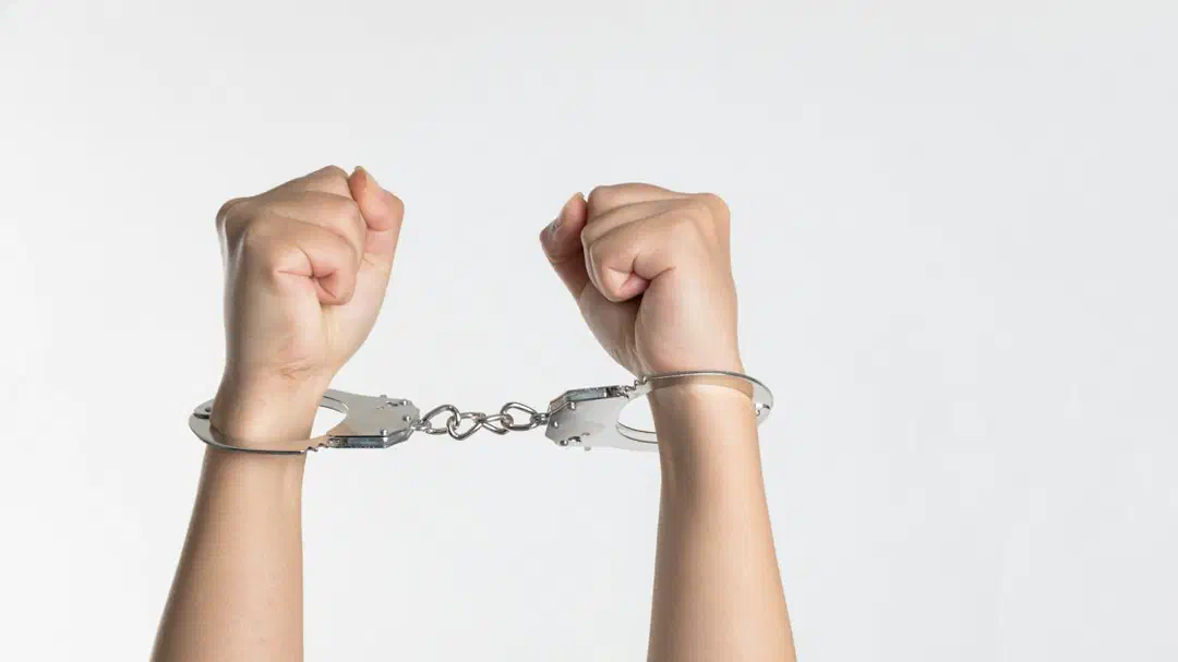 A pair of wrists held up in handcuffs against a white background