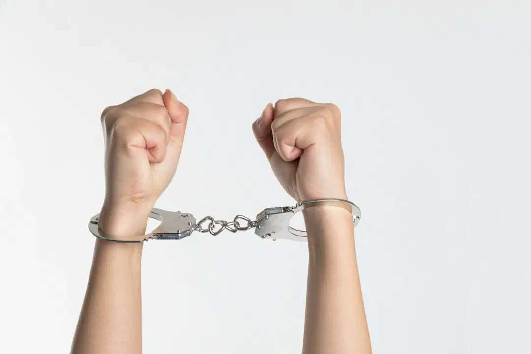 A pair of wrists held up in handcuffs against a white background