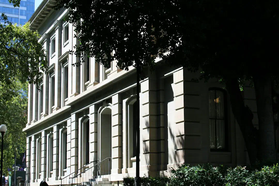 A historic stone building with columns surrounded by green trees and grass