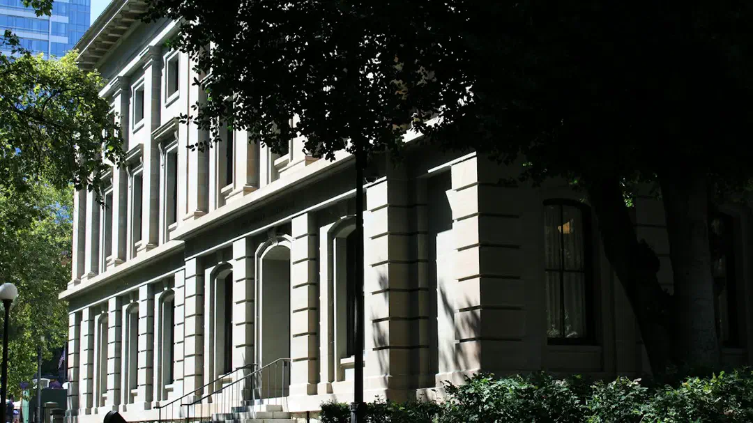 A historic stone building with columns surrounded by green trees and grass