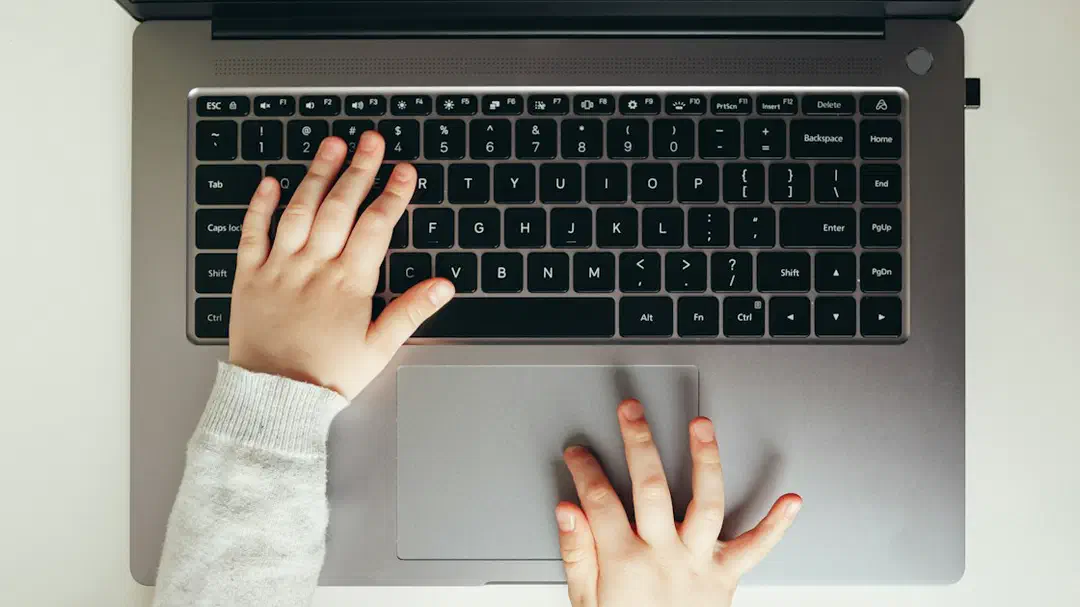 A child's hands typing on a laptop keyboard, seen from above