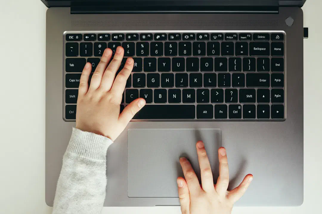 A child's hands typing on a laptop keyboard, seen from above