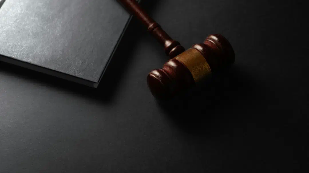A wooden gavel beside a closed black book on a dark surface