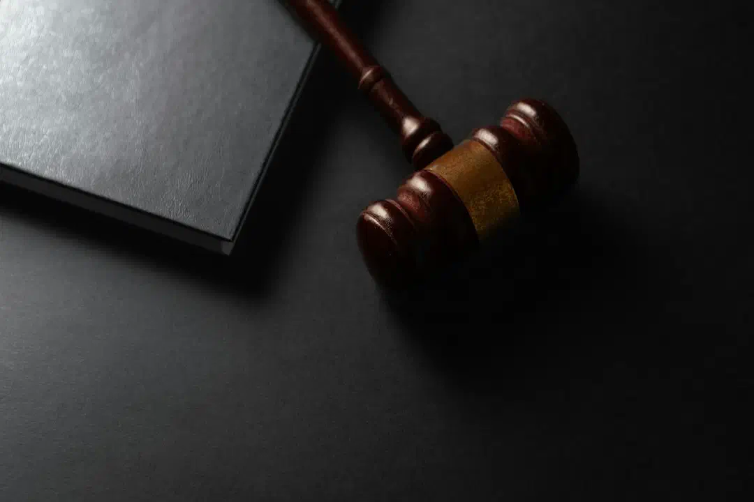 A wooden gavel beside a closed black book on a dark surface